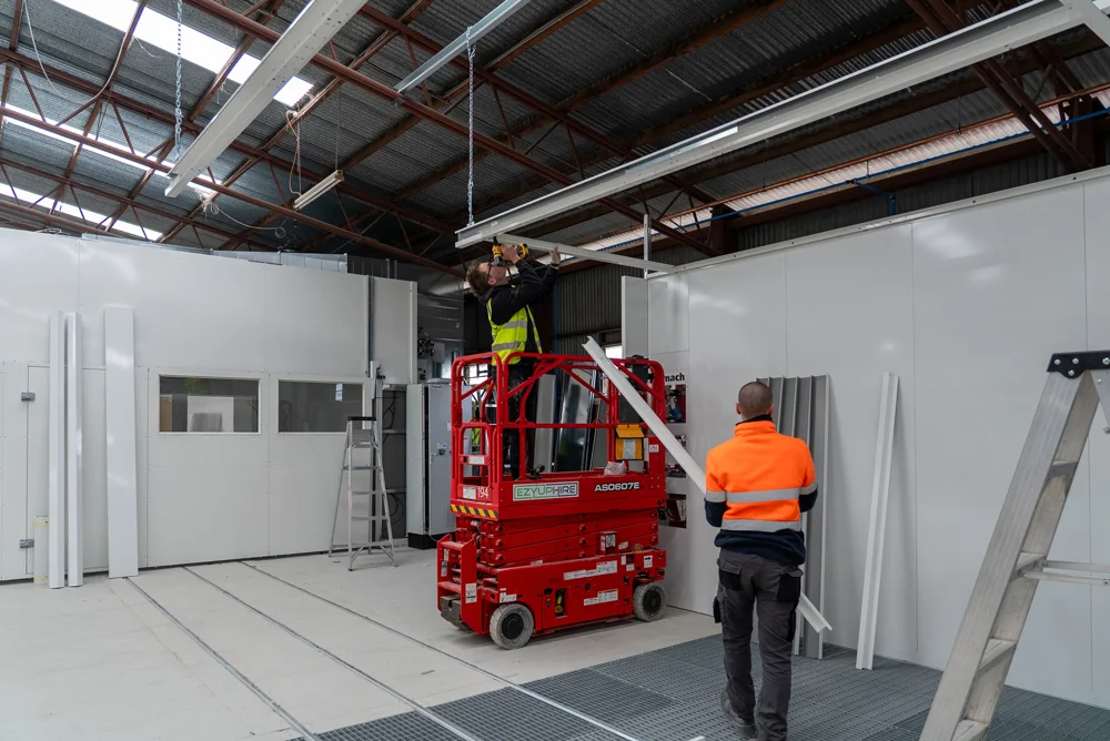 Large industrial workspace with workers installing equipment using a red scissor lift.